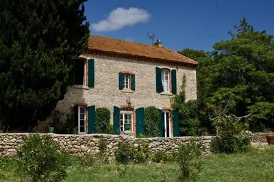 a stone house with green shutters and a stone wall at Maison Saraphina in Cruzy