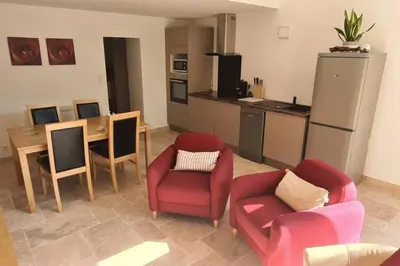 a living room with two chairs and a table and a kitchen at Ruby - Gîte 2 chambres dans vieux prieuré près de Carcassonne in Sainte-Eulalie