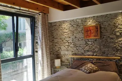a bedroom with a stone wall with a bed and a window at Diamond - Gîte dans vieux prieuré près de Carcassonne in Sainte-Eulalie