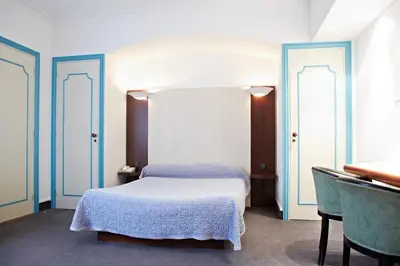 a bedroom with a white bed and two windows at Hôtel Mets et Plaisirs in Mazamet