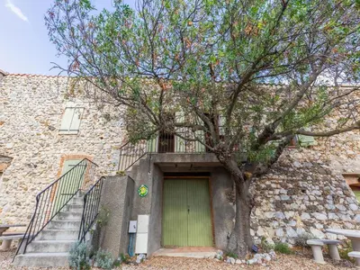 a stone building with a green door and a tree at Charming Holiday Home in Tautavel with Balcony in Tautavel