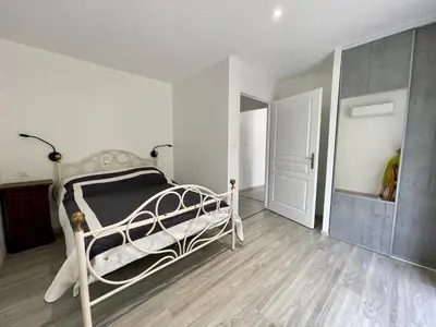 a bedroom with a white bed and a wooden floor at Le Fenouillet Cottage proche des Grands Buffets in Narbonne