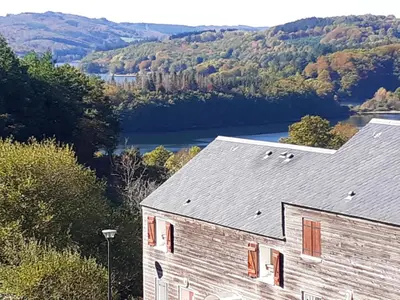 a building with a view of a river and trees at Gîte du Gua des Brasses au bord du lac de la Raviège in La Salvetat