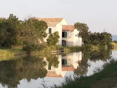 a house on a lake with its reflection in the water at MOBILHOME agréable sans draps ni serviettes in Port-la-Nouvelle