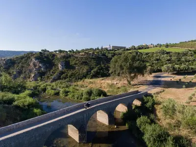 a bridge over a river with two people on it at Château de Lastours - Le Resort in Portel-des-Corbières