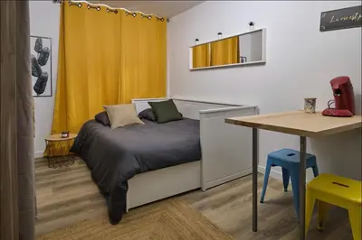 a bedroom with a bed and a table and yellow curtains at Chez Juliette - Appart & Studios - Carcassonne centre in Carcassonne