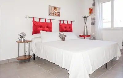 a cat sitting on a white bed with red pillows at 2 Bedroom Cozy Home In Saint Chinian in Saint-Chinian