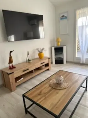 a living room with a table and a tv on the wall at New Maison tout confort, bord de mer avec Parking Privé in Gruissan