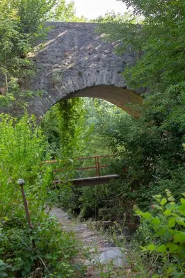 a stone bridge over a trail with a bench under it at Gîte Roc Suzadou in Ferrals-les-Montagnes