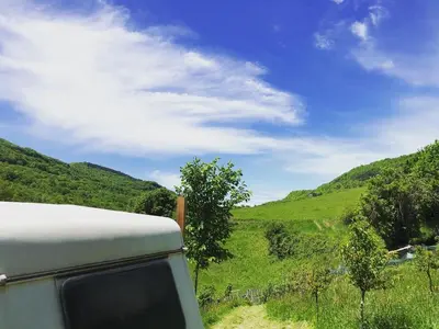 a camper van parked on a dirt road with green hills at Gîte Aurinko : caravane avec bain nordique in Roquefort-les-Cascades