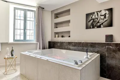 a large bath tub in a bathroom with a window at Les Gîtes de Laure - O Lit Divin, Instant de volupté, BALNEO SAUNA, Climatisation, Netflix, 160m de la Cité Médiévale in Carcassonne