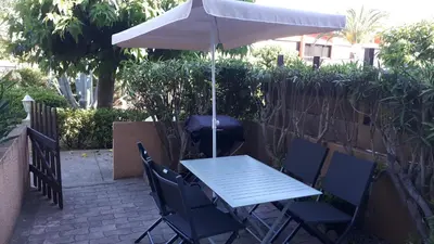 a table and chairs with an umbrella on a patio at Studio cabine avec jardinet à 30 m de la plage, au calme. in Gruissan