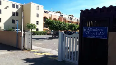 a white fence with a sign on it next to a parking lot at Studio cabine avec jardinet à 30 m de la plage, au calme. in Gruissan