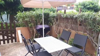 a table and chairs with an umbrella on a patio at Studio cabine avec jardinet à 30 m de la plage, au calme. in Gruissan