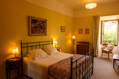 a bedroom with a bed and a chair and a window at The Riverside Gîte Lagrasse in Lagrasse