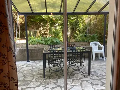 a patio with a table and a bench and a blue canopy at Maison DELMAS, l'Oustal du Recantu in Sainte-Eulalie