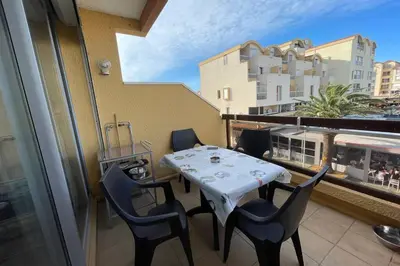 a table and chairs on a balcony with a train at Appartement terrasse sur le port, piscine, tennis in Gruissan