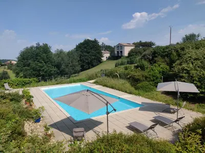 a swimming pool with chairs and an umbrella and a house at Gites Arnoult in Damiatte