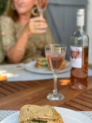 a woman sitting at a table with a sandwich and a wine glass at Pavillon confort pour 2 personnes GRUISSAN in Gruissan