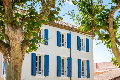 a house with blue shutters and a tree at Maison d'hôtes ÔVillage in Ouveillan