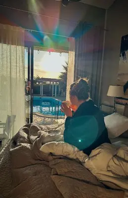 a woman sitting on a bed looking out a window at Marie Jean Chambre d'hôtes & Gîte in Oupia