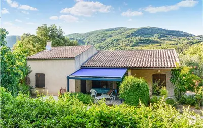 a house with a blue awning and mountains in the background at 2 Bedroom Awesome Home In Berlou in Berlou