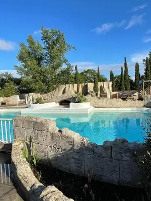 a swimming pool with blue water and a stone wall at Gîte-appart privé du Domaine Spa piscine sauna in Lescout