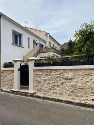a white house with a stone wall and a gate at L'esplanade, appartement en centre-ville au calme in Puisserguier