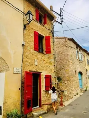 a person standing outside of a building with red shutters at Jolie maison village 4 couchages &Terrasse à Fitou in Fitou