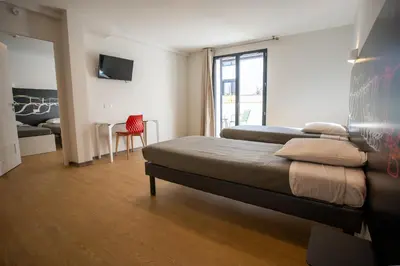a bedroom with two beds and a red chair at CIS Lamourelle Centre International de Sejour in Carcassonne