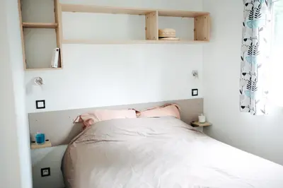 a small bedroom with a bed with white sheets at Mobil Home XXL 4 chambres - Camping Le Barberousse in Gruissan