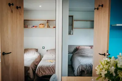 a bedroom with two beds and a door with a mirror at Mobil Home XXL 4 chambres - Camping Le Barberousse in Gruissan