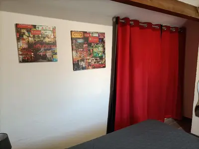 a bedroom with a red curtain and pictures on the wall at L'Appart de Karine et Nico in Gruissan