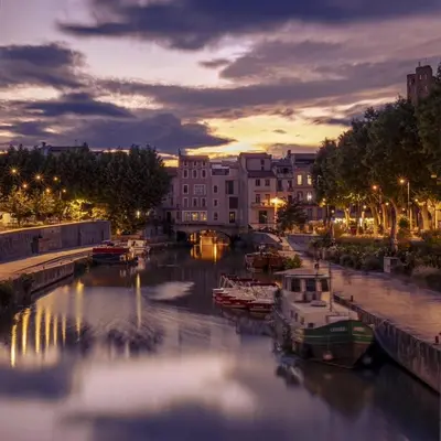 a group of boats docked in a river at night at Le trois nourrices in Narbonne
