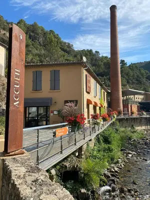 a building with flowers on a bridge next to a river at 3 Star 3 bed Air Conditioned QUERTINEUX 100m to Historic 4 Cathar Châteaux Lastours access to a very Pretty Riverside Garden!! in Lastours