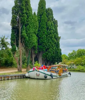 a boat is docked on the water next to trees at Bijou SURDESPINE air conditioned 100m to Historic 4 Cathar Châteaux Lastours access to a very pretty riverside garden!! in Lastours