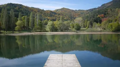 a dock on a lake with trees and mountains at L'Oustal des amis in Belcaire