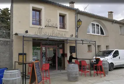 a person standing outside of a restaurant with red chairs at La Maison de Leontine in La Livinière