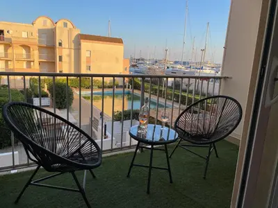 a balcony with two chairs and a table with a wine glass at T3 Expo Sud-Est - Parking - Piscine - Clim - Wifi in Gruissan