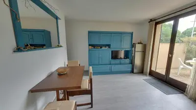 a kitchen with blue cabinets and a table and a refrigerator at Gruissan: Maisonnette T2 avec jardin in Gruissan