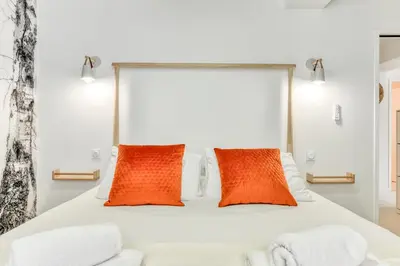 a bedroom with a white bed with two orange pillows at Les Gîtes de Laure - L'Or Blanc, Appartement avec Vue sur le Chateau, Climatisation, Netflix, à 160 m de la Cité Médiévale in Carcassonne