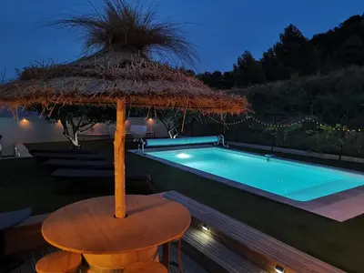 a table with a straw umbrella next to a swimming pool at Maison L'Inattendu avec spa & piscine privatifs in Moussan