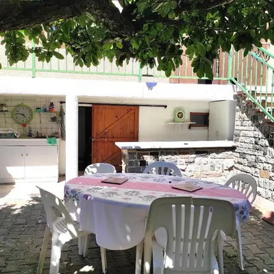 a table with white chairs and a kitchen in a backyard at Villa Aimé in Caunes-Minervois