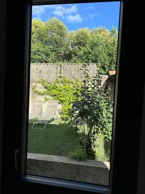 a window view of a yard with a tree and chairs at Le Marceau - Maison climatisée avec jardin in Carcassonne