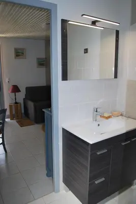 a bathroom with a sink and a mirror and a living room at Au Canalet - Le Somail in Le Somail