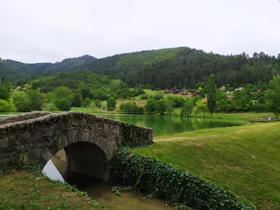 a stone bridge over a lake with a mountain at Belle maison proche de la ville et du lac in Belcaire