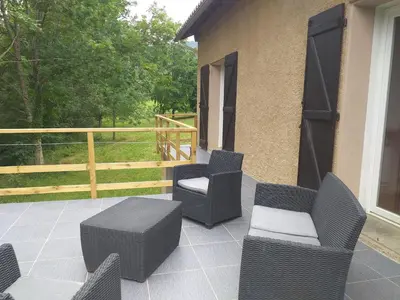 a patio with wicker chairs and tables and a fence at Belle maison proche de la ville et du lac in Belcaire