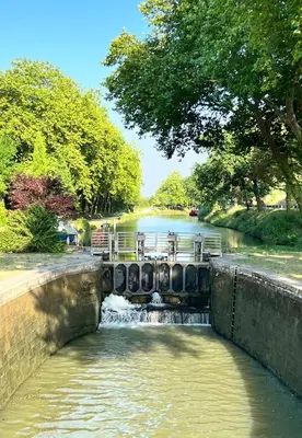 a small river with water flowing through a bridge at Péniche Dondon - Gîte cocooning sur Canal du midi in Avignonet-de-Lauragais