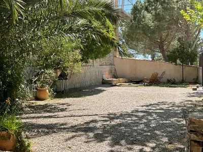 a backyard with a wall and a chair and trees at Joli gîte chic et cosy entre mer et Narbonne in Narbonne