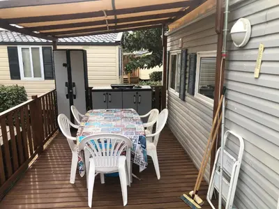 a table and chairs on a deck with a grill at Cathy & David-Mobile Home 11-Camping Novela in Port-la-Nouvelle
